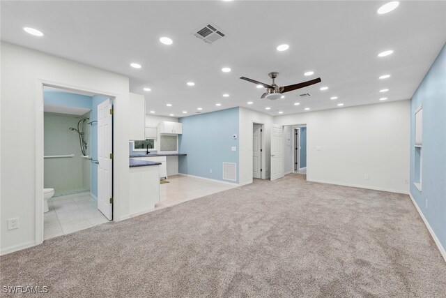 unfurnished living room with ceiling fan, light carpet, and sink