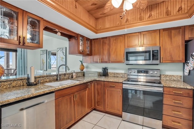 kitchen with light stone countertops, stainless steel appliances, a tray ceiling, sink, and light tile patterned floors