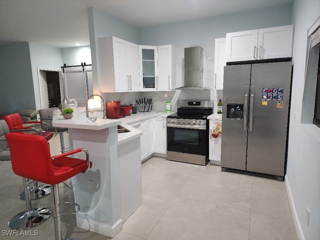 kitchen with wall chimney range hood, kitchen peninsula, a breakfast bar, a barn door, and appliances with stainless steel finishes