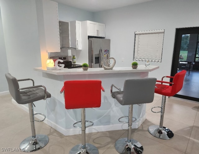 kitchen featuring appliances with stainless steel finishes, wall chimney range hood, kitchen peninsula, a kitchen breakfast bar, and white cabinetry