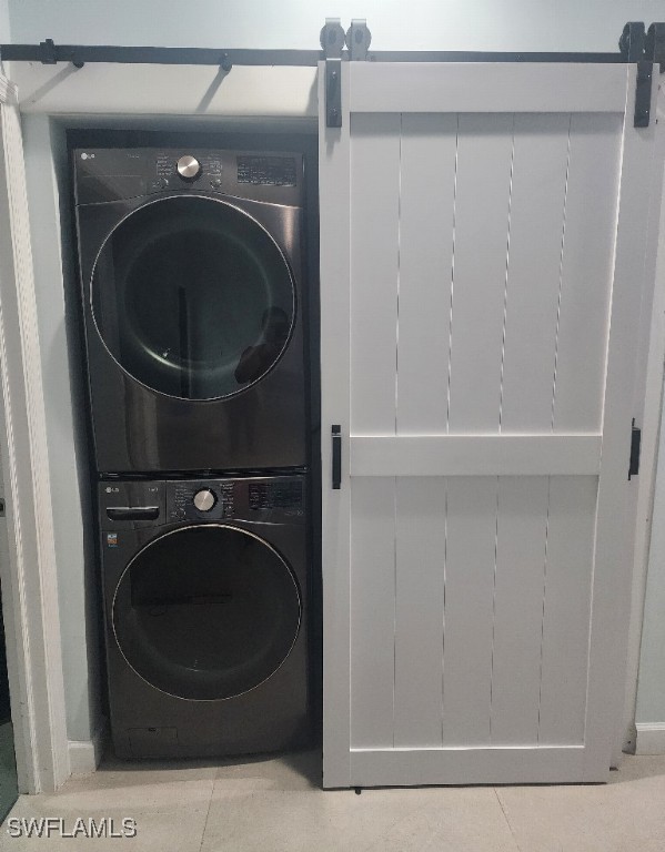 washroom featuring stacked washer / dryer, tile patterned flooring, and a barn door