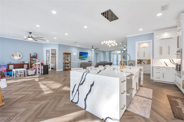 kitchen with a kitchen island with sink, light parquet floors, ceiling fan, decorative light fixtures, and white cabinetry