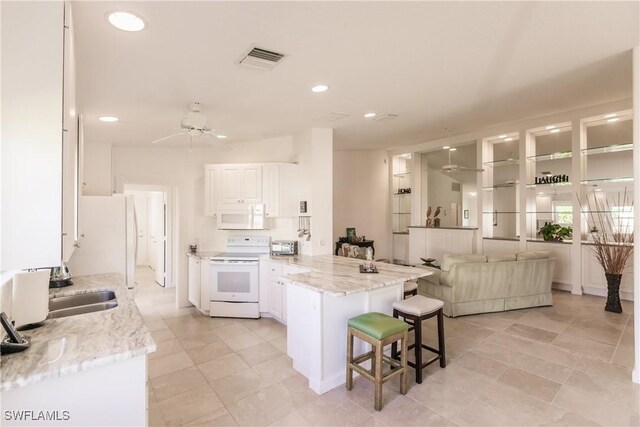 kitchen featuring white cabinets, ceiling fan, a breakfast bar, light stone counters, and white appliances