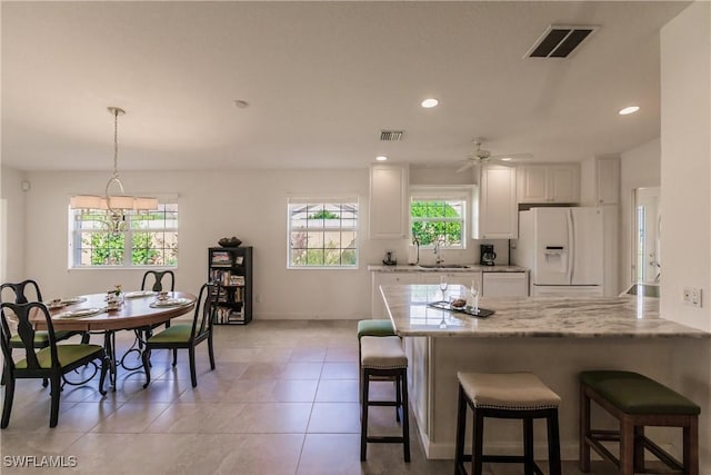 kitchen with visible vents, white fridge with ice dispenser, white cabinetry, pendant lighting, and a sink