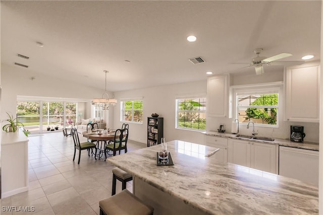 kitchen with light stone counters, decorative light fixtures, visible vents, white cabinets, and a sink