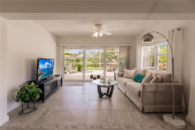 living room featuring a ceiling fan, a wealth of natural light, baseboards, and light tile patterned floors