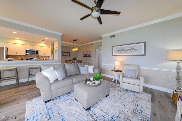 living room featuring light hardwood / wood-style flooring, ceiling fan with notable chandelier, and crown molding