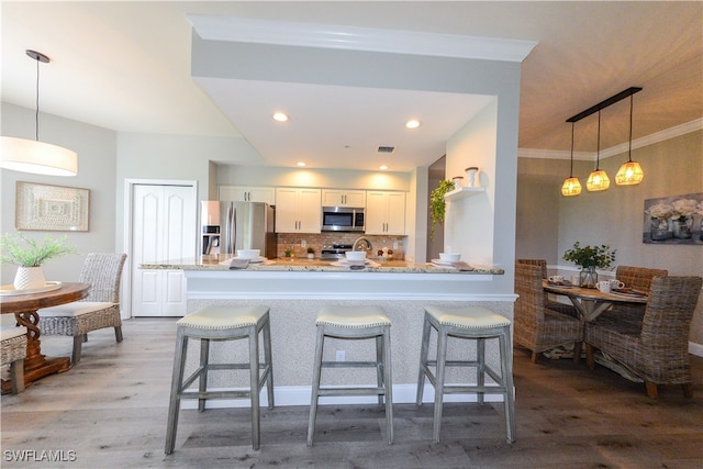 kitchen with kitchen peninsula, hardwood / wood-style floors, appliances with stainless steel finishes, white cabinetry, and decorative light fixtures