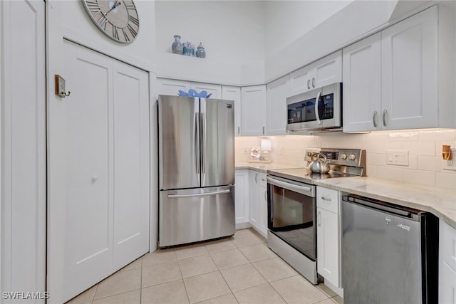 kitchen featuring light stone countertops, decorative backsplash, stainless steel appliances, white cabinets, and light tile patterned floors