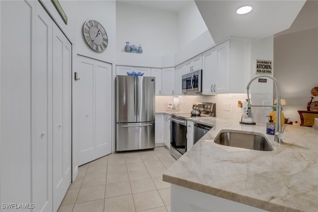 kitchen featuring light stone countertops, stainless steel appliances, sink, white cabinetry, and light tile patterned floors