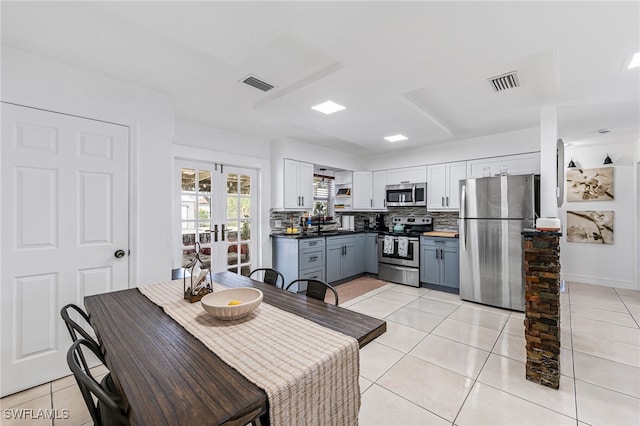 kitchen featuring white cabinets, light tile patterned floors, tasteful backsplash, gray cabinets, and appliances with stainless steel finishes