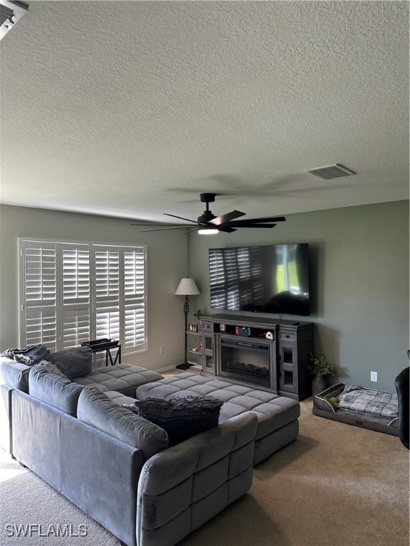 carpeted living room featuring ceiling fan and a textured ceiling