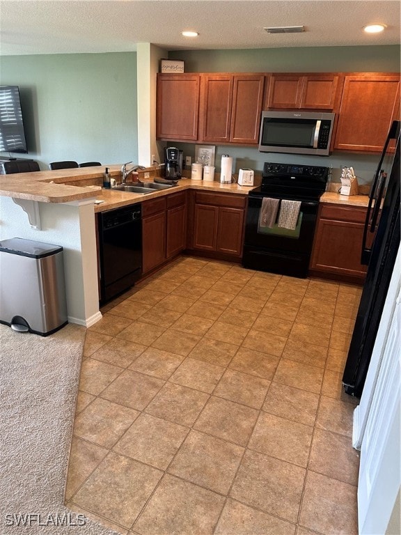 kitchen with sink, kitchen peninsula, a textured ceiling, a breakfast bar, and black appliances