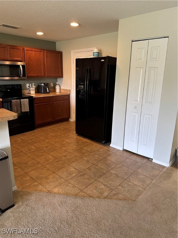 kitchen featuring light colored carpet, black appliances, and a textured ceiling