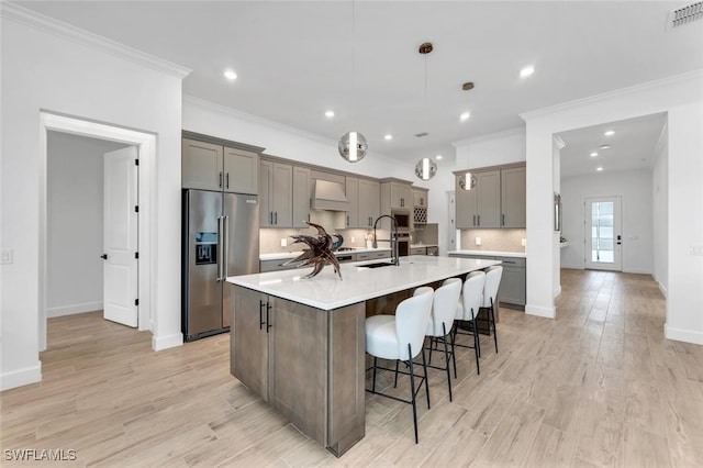 kitchen with hanging light fixtures, high end refrigerator, a kitchen island with sink, light hardwood / wood-style flooring, and custom range hood