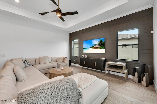 living room featuring ceiling fan, wood walls, ornamental molding, and light wood-type flooring