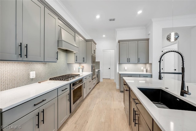 kitchen with light hardwood / wood-style flooring, stainless steel appliances, ornamental molding, sink, and premium range hood