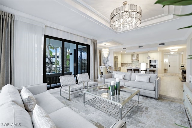 living room featuring a raised ceiling, ornamental molding, and an inviting chandelier