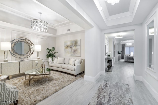 living room with a tray ceiling, an inviting chandelier, and light hardwood / wood-style floors