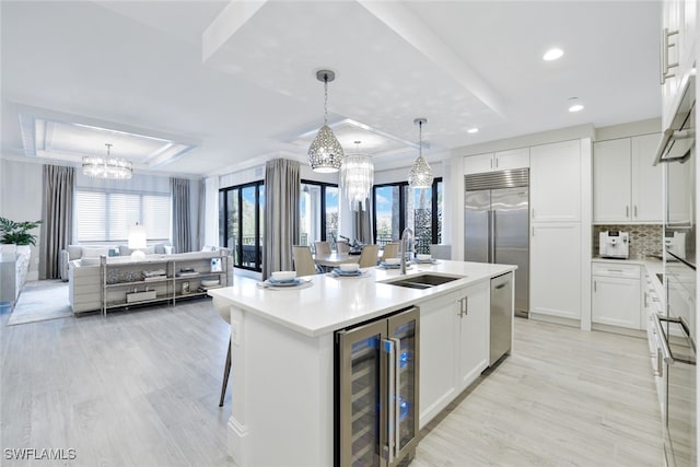 kitchen featuring white cabinets, a center island with sink, sink, light hardwood / wood-style flooring, and beverage cooler