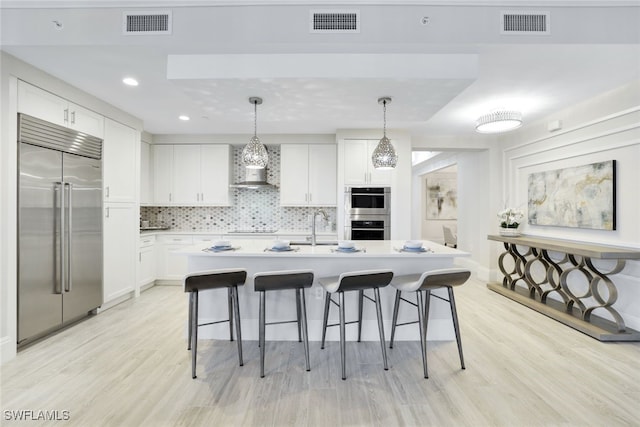 kitchen featuring white cabinetry, wall chimney exhaust hood, light hardwood / wood-style floors, pendant lighting, and appliances with stainless steel finishes