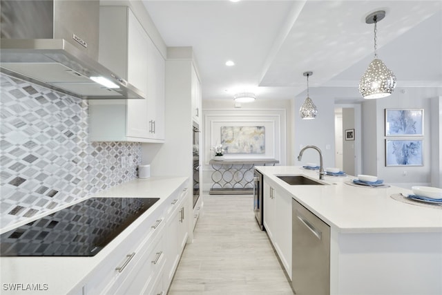 kitchen featuring dishwasher, black electric stovetop, wall chimney exhaust hood, an island with sink, and decorative light fixtures