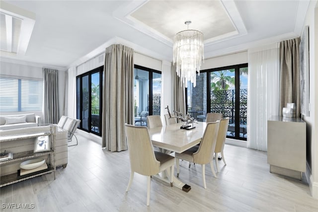 dining space with light hardwood / wood-style floors, an inviting chandelier, a wealth of natural light, and a tray ceiling