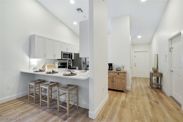 kitchen with white cabinets, a kitchen breakfast bar, light wood-type flooring, and stainless steel appliances