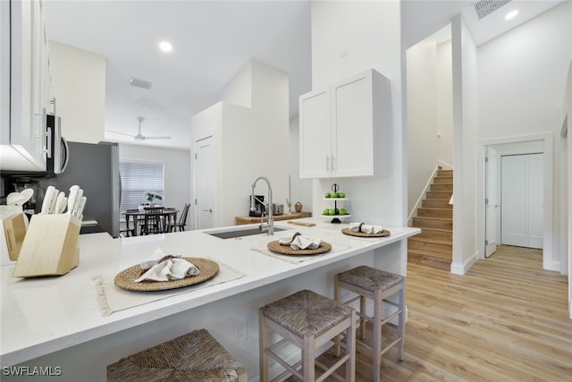 kitchen with ceiling fan, sink, a kitchen breakfast bar, kitchen peninsula, and white cabinets