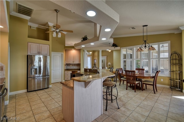 kitchen with light brown cabinets, light tile patterned flooring, stainless steel fridge with ice dispenser, a breakfast bar, and light stone countertops