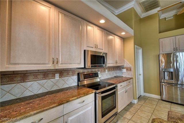 kitchen with light tile patterned floors, appliances with stainless steel finishes, dark stone countertops, crown molding, and decorative backsplash