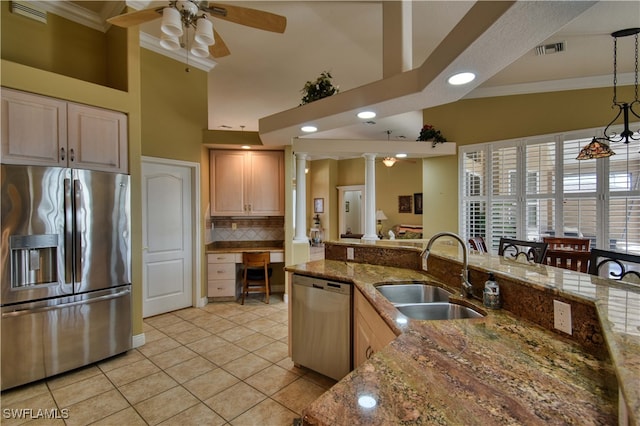 kitchen with dark stone countertops, sink, light brown cabinetry, appliances with stainless steel finishes, and decorative columns