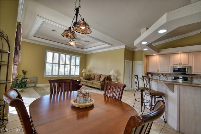 tiled dining area with crown molding and a tray ceiling