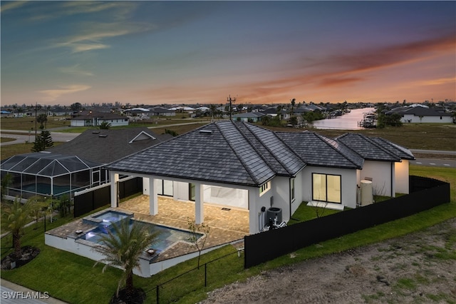 back house at dusk featuring central air condition unit, a fenced in pool, a water view, a patio area, and glass enclosure