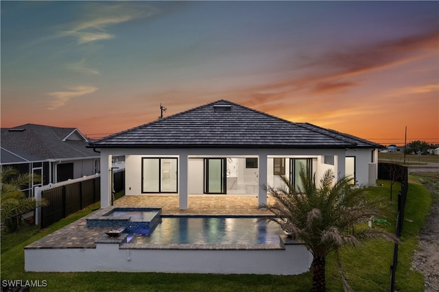 back house at dusk featuring a patio and a pool with hot tub