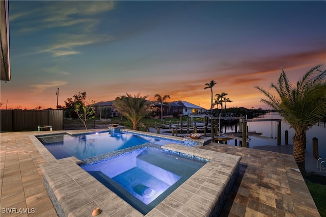 pool at dusk with a patio area, an in ground hot tub, and a water view