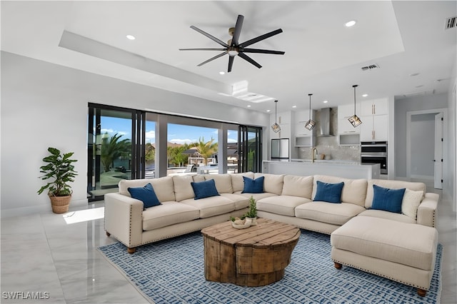 living room with sink, ceiling fan, and a tray ceiling