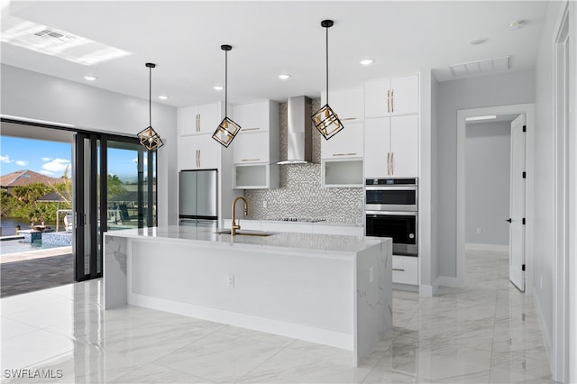 kitchen with a kitchen island with sink, wall chimney exhaust hood, sink, white cabinets, and appliances with stainless steel finishes