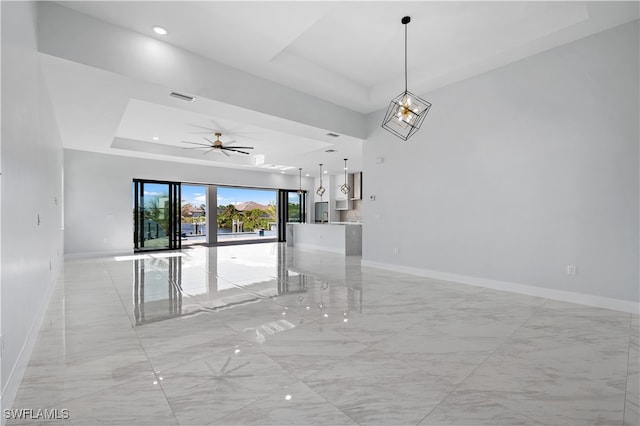 empty room featuring ceiling fan with notable chandelier and a raised ceiling