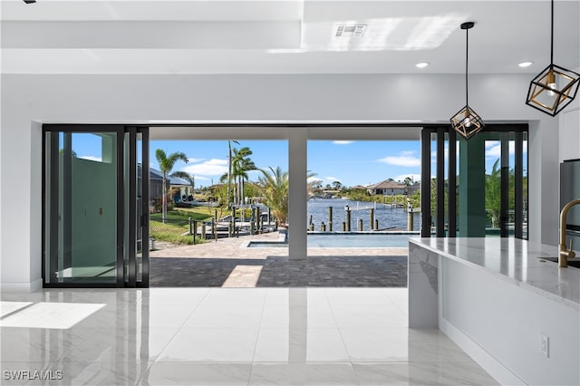 interior space with pendant lighting, light stone counters, a water view, and a healthy amount of sunlight