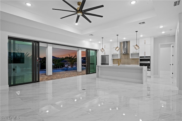 kitchen featuring an island with sink, backsplash, white cabinets, decorative light fixtures, and appliances with stainless steel finishes