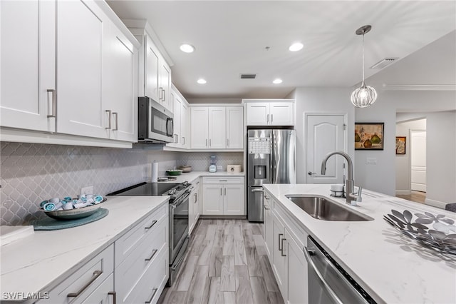 kitchen featuring hanging light fixtures, sink, white cabinetry, appliances with stainless steel finishes, and decorative backsplash