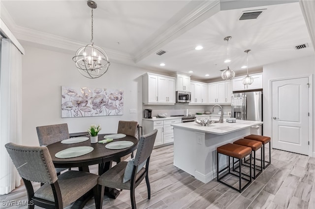 kitchen featuring appliances with stainless steel finishes, pendant lighting, an island with sink, and white cabinets