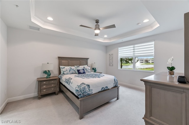 bedroom with ceiling fan, a tray ceiling, ornamental molding, and light carpet