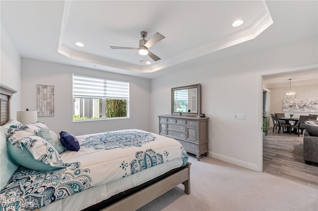 bedroom featuring ornamental molding, ceiling fan with notable chandelier, light wood-type flooring, and a tray ceiling