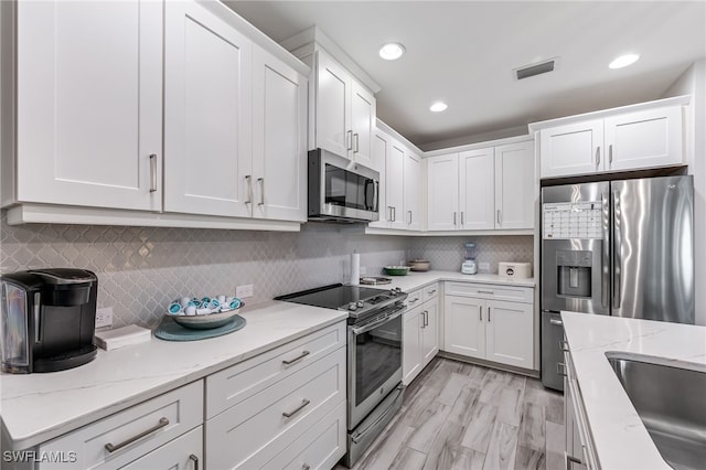 kitchen featuring light stone countertops, decorative backsplash, white cabinetry, and stainless steel appliances