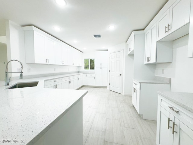 kitchen featuring light stone countertops, sink, and white cabinetry