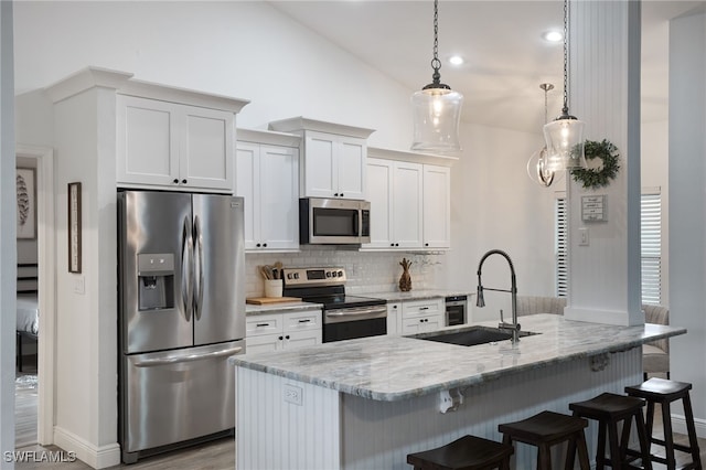 kitchen with stainless steel appliances, a center island with sink, light stone countertops, decorative light fixtures, and white cabinets