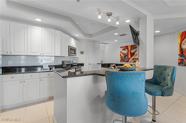 kitchen with a tray ceiling, a breakfast bar, white cabinetry, light tile patterned floors, and appliances with stainless steel finishes