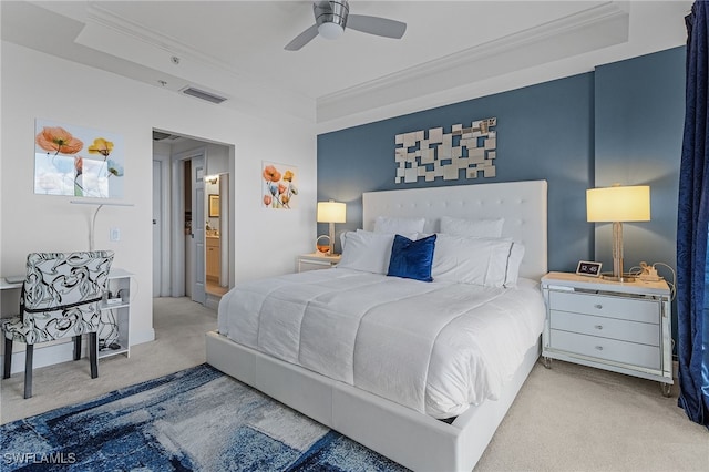 bedroom featuring ensuite bath, ornamental molding, light colored carpet, a raised ceiling, and ceiling fan